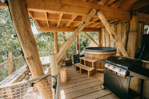Terraza de casa en el árbol con tina de madera y barbacoa en Cosy Cabins, bosque de Limburgo, Bélgica.