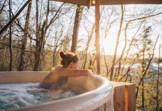 Woman relaxing in an outdoor hot tub at Cosy Cabins in the forest of Limburg, Belgium, at sunset.
