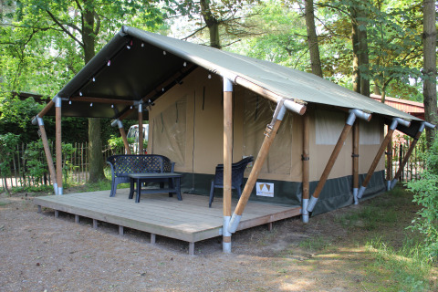 Tienda safari con terraza de madera y muebles de exterior, situada en un entorno arbolado para glamping.