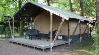 Tienda safari con terraza de madera y muebles de exterior, situada en un entorno arbolado para glamping.