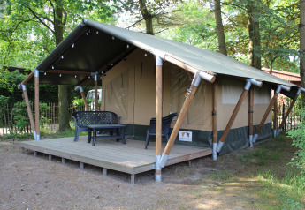 Tienda safari con terraza de madera y muebles de exterior, situada en un entorno arbolado para glamping.