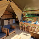 Interno di tenda safari con mobili in legno, tavolo da pranzo e angolo cottura a Domaine La Sauzette, Francia.