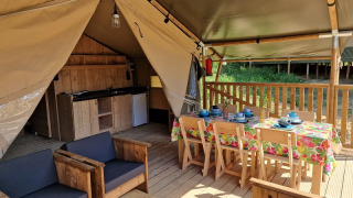 Interior of safari tent with wooden furniture, dining table, and kitchenette at Domaine La Sauzette, France.