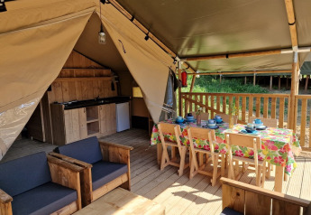 Interior of safari tent with wooden furniture, dining table, and kitchenette at Domaine La Sauzette, France.