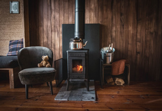 Cozy wooden cabin interior in Limburg forest, Belgium, with wood stove, armchair, and teddy bear.
