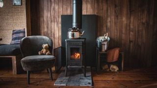 Gemütliche Holzhütte mit Kaminofen, Sessel und Teddybär im Wald von Limburg, Belgien.