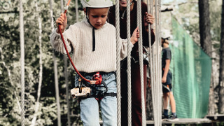 Kind und Erwachsener mit Helm und Gurt auf einem Hochseilpark bei Cosy Cabins im Wald von Limburg.