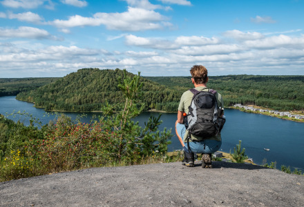 Person mit Rucksack blickt auf einen See und Glamping-Unterkünfte in einem naturnahen Ferienpark.