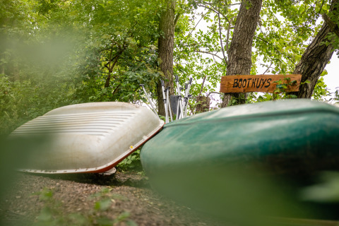 Two canoes rest beside a wooden 'Boothuys' sign amid green foliage at Buitengoed Ruysbos holiday park.