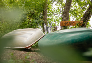 Two canoes rest beside a wooden 'Boothuys' sign amid green foliage at Buitengoed Ruysbos holiday park.