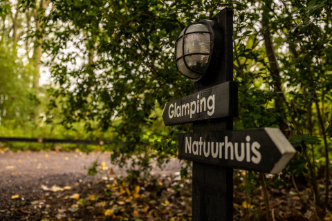 Skilt med retninger til Glamping og Naturhus, omgivet af grønt, i Buitengoed Ruysbos, Gelderland.
