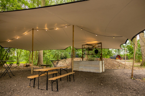 Zona de picnic al aire libre con bancos y mesas bajo una carpa, situada en el bosque de Buitengoed Ruysbos