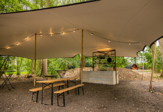 Outdoor picnic area with benches and tables under a canopy, located in the forest at Buitengoed Ruysbos