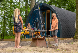 Two children cook over an outdoor fire in front of a cabin at Buitengoed Ruysbos, Gelderland, Netherlands.