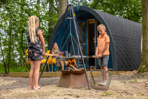 Twee kinderen bereiden eten op een kampvuur voor een hut in Buitengoed Ruysbos, Gelderland, Nederland.