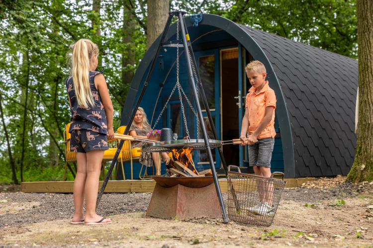 Two children cook over an outdoor fire in front of a cabin at Buitengoed Ruysbos, Gelderland, Netherlands.