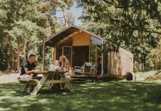 Gezin geniet van picknick aan houten tafel voor moderne vakantiewoning in het groen bij Beerze Bulten.