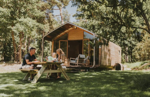 Gezin geniet van picknick aan houten tafel voor moderne vakantiewoning in het groen bij Beerze Bulten.