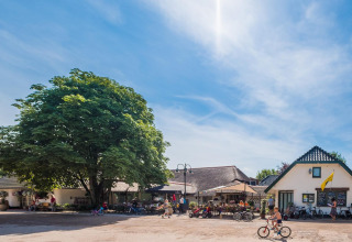 Zonnige dag bij Camping Vossenberg in Gelderland, Nederland, met kinderen op fietsen en terrasgasten buiten.