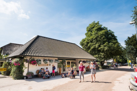 Familie geniet van een zonnige dag bij Camping Vossenberg in Gelderland, Nederland, met huisjes en bomen.