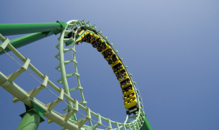 Montaña rusa haciendo un loop en parque vacacional con glamping, cielo despejado y pasajeros emocionados.