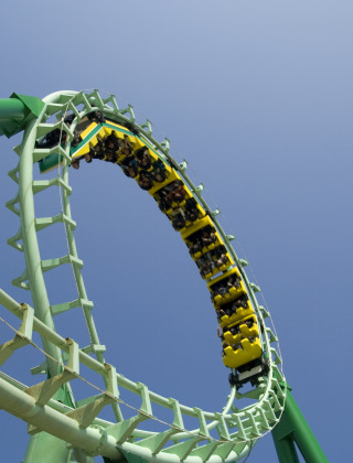 Roller coaster looping high in a holiday park that offers glamping, with excited riders and clear blue sky.