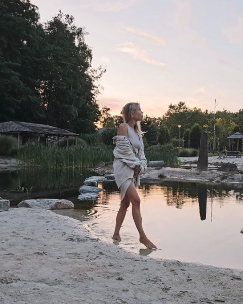 Mujer camina junto al agua al atardecer en Cosy Cabins, un parque vacacional en el bosque de Limburg, Bélgica.