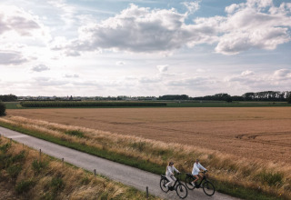 Two people cycle along a rural path near fields and forest at Cosy Cabins holiday park, Limburg, Belgium.
