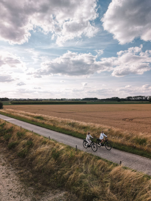 Due persone in bicicletta lungo una strada rurale tra i campi presso Cosy Cabins, Limburgo, Belgio.