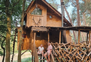 Two men sit on the stairs of a rustic tree cabin at Cosy Cabins forest holiday park in Limburg, Belgium.