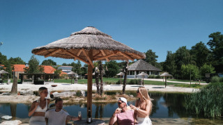 Vier mensen ontspannen onder een parasol op het zand bij Cosy Cabins in Limburg, België.