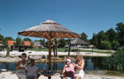 Quattro persone si rilassano sotto un ombrellone di paglia sulla spiaggia di Cosy Cabins a Limburg, Belgio.