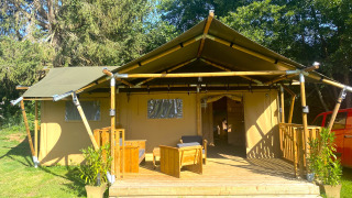 Safari tent with wooden deck and seating at Moulin du Pommier Glamping & Camping in France, surrounded by greenery.