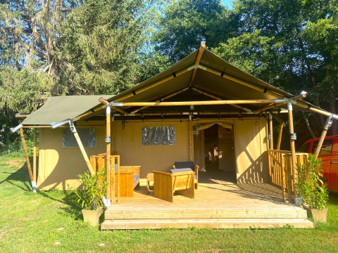 Safari tent with wooden deck and seating at Moulin du Pommier Glamping & Camping in France, surrounded by greenery.