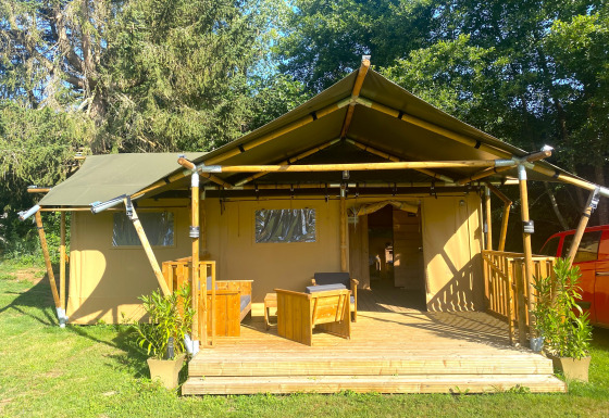 Safari tent with wooden deck and seating at Moulin du Pommier Glamping & Camping in France, surrounded by greenery.
