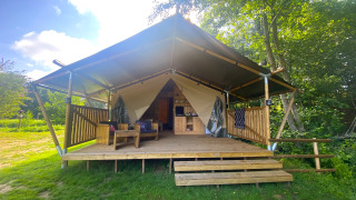 Tenda safari con veranda in legno al Moulin du Pommier Glamping & Camping in Francia, immersa nel verde.