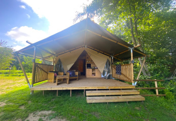 Tenda safari con veranda in legno al Moulin du Pommier Glamping & Camping in Francia, immersa nel verde.