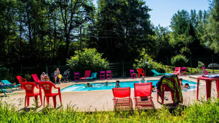Niños jugando en una piscina exterior rodeada de sillas de colores en Camping Les Bouleaux, Grand Est, Francia.