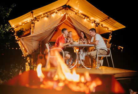 Cuatro amigos cenan juntos frente a una tienda iluminada y una fogata cerca de Vilsberg, Grand Est, Francia.