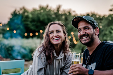 Twee lachende vrienden genieten van een drankje buiten bij TinyParks Cast Away in Zuid-Holland, Nederland.