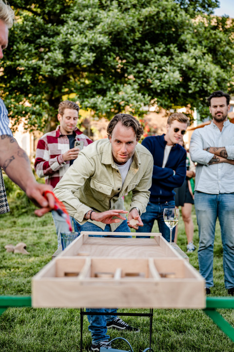 Een groep vrienden speelt een houten tafelspel buiten op het gras bij TinyParks Cast Away in Zuid-Holland.