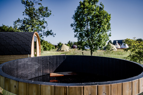 Ronde houten hot tub en sauna op een zonnig veld bij TinyParks Cast Away, Zuid-Holland, Nederland.