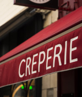 Red awning with the word 'CREPERIE' in white, seen outside a building likely serving French crepes.