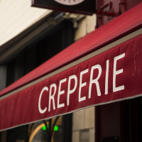 Toldo rojo con la palabra 'CREPERIE' en blanco, visto frente a un local que probablemente sirve crepas.