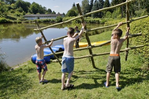 Drie kinderen bouwen samen een vlot aan de oever van een meer bij Camping Donnersberg, Duitsland.