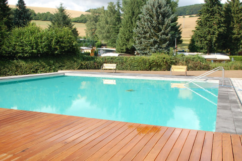 Een buitenzwembad met houten terras in een rustige, groene omgeving bij Camping Donnersberg, Duitsland.