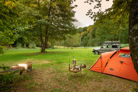 Kampeerplek bij Camping Donnersberg met oranje tent, Land Rover, en groene natuur in Duitsland.