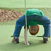 Junge steht kopfüber auf dem Minigolfplatz