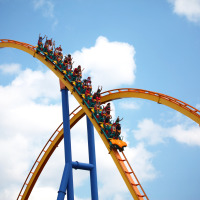 Personas disfrutan una montaña rusa en un parque vacacional con opciones de glamping y cielo azul.
