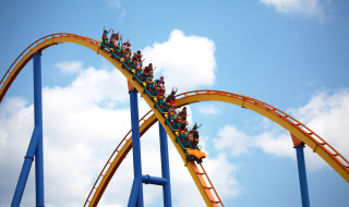 Menschen fahren auf einer Achterbahn im Freizeitpark mit Glamping-Angeboten unter blauem Himmel.